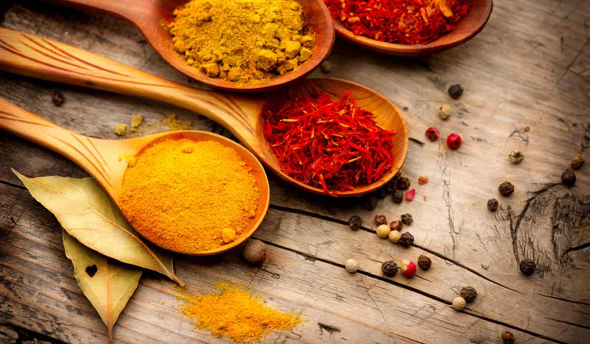 Overhead shot of wooden spoons holding colorful spices like turmeric, saffron and chili flakes on a rustic wood surface
